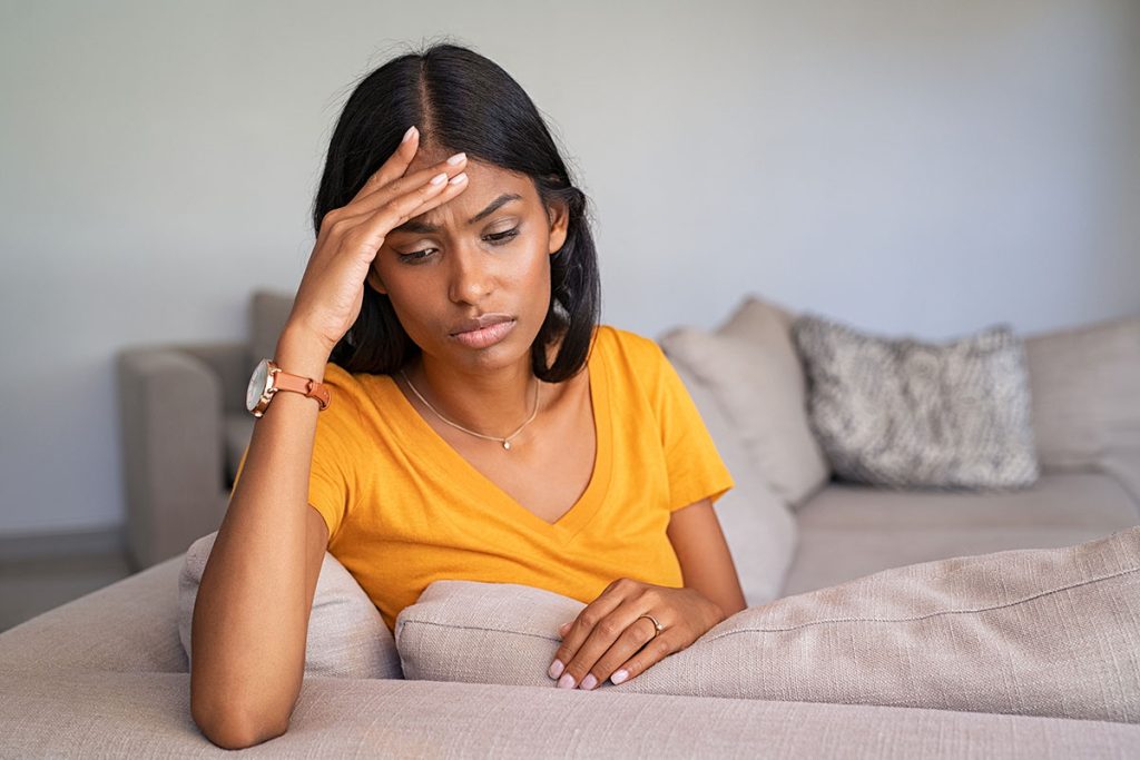 A woman sitting on the bed with her head in her hand.