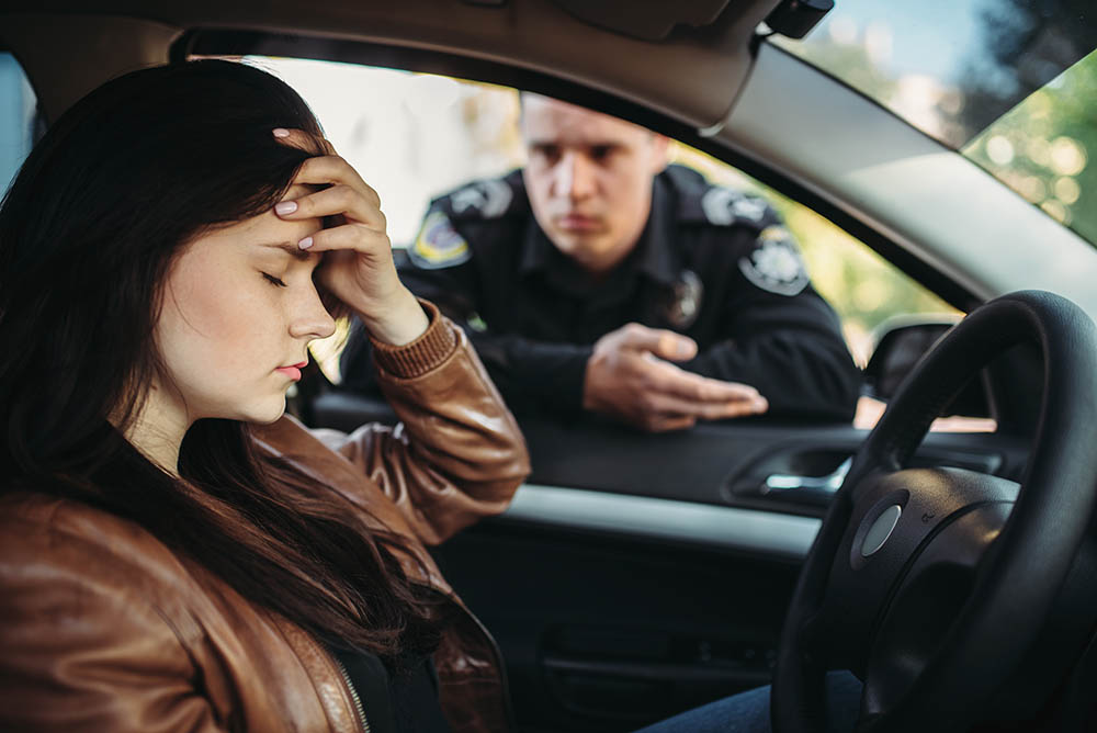 A woman sitting in the driver 's seat of a car while another man sits behind her.