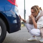 A woman squatting down to inspect the tire of her car.