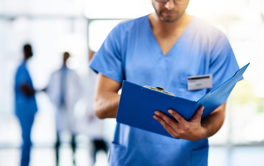 A man in scrubs holding a blue folder.